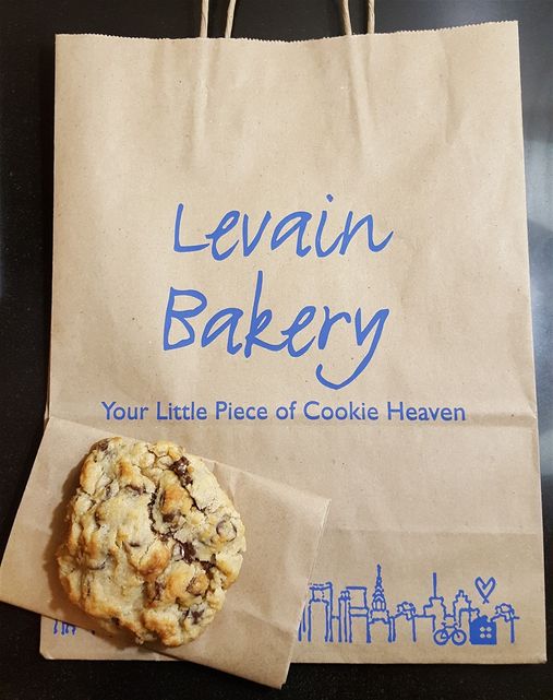 A composition of a walnut chocolate chip cookie and the beautifully crafted Lavain paper bag.