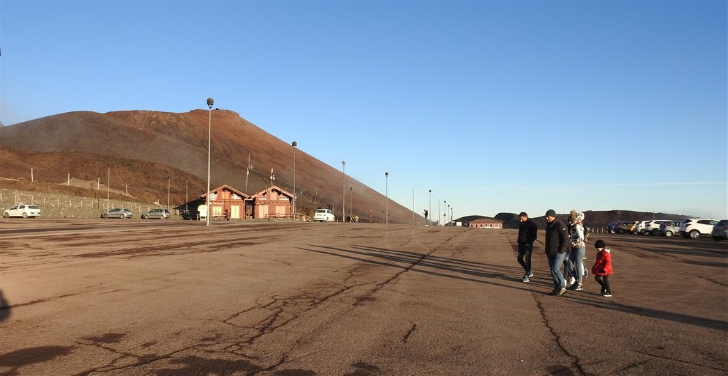 The huge car parking lot at Rifugio Sapienza.  The redish cone on the left is the big crater of the Upper Crateri Silvestri. The lower 