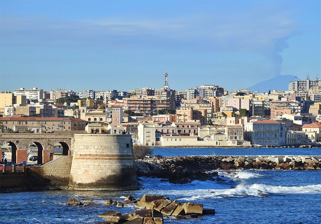 View over the city to the north, beyond Ortygia, and the Mount Etna in the background smoking.