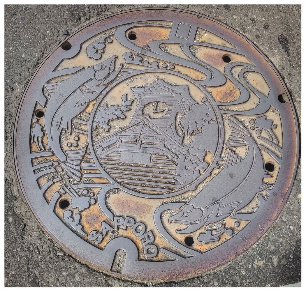 Sapporo sewer cover depicts the Sapporo Clock Tower and a pair of salmon.