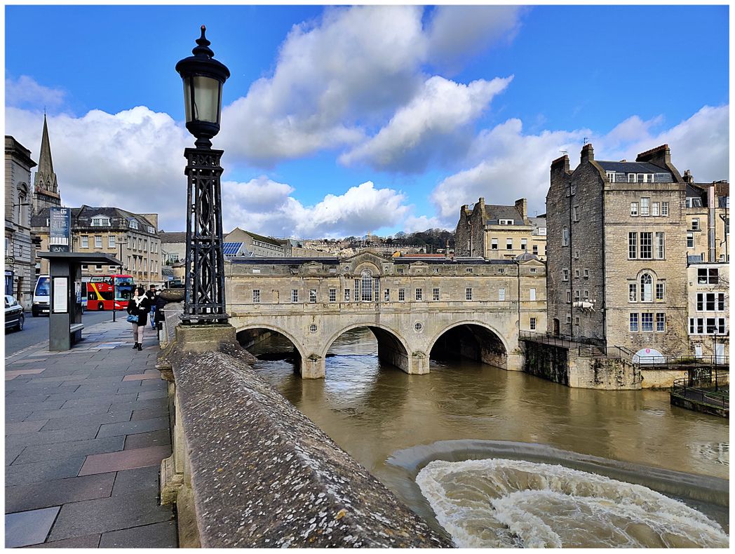The Pulteney Bridge. One of the most photographed examples of Georgian architecture in the city and one of only four bridges in the world to have shops across its full span on both sides, Pulteney Bridge was designed in 1769 by Robert Adam.  The bridge is named after Frances Pulteney, wife of William Johnstone Pulteney. William was an important man in Georgian Bath, owning a lot of land in the surrounding area. He had grand plans to create a 'new town' to rival that of John Wood's on the west side of the city.   His grand scheme needed a new bridge and he didn't want just any old bridge, he wanted a spectacular bridge, one which everyone would talk about. The architecture is classical, with pediments, pilasters and tiny leaded domes at either end.  The shops are small and the roadway is not wide, but when the bridge opened in 1770 it was a revelation. Today it is surely one of the world's most beautiful and romantic bridges, best viewed from Parade Gardens and the crescent weir.  Famously, it was the scene of Javert's suicide in the 2012 film version of Les Misérables.