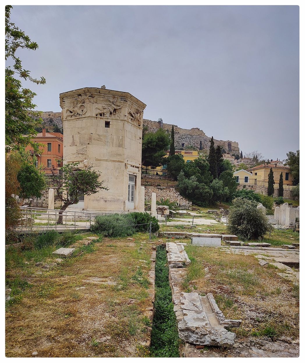 The public latrines (Vespasianae) can be seen in the foreground.  The Tower of the Winds stands behide them, and the Acropolis can be seen at the background.
